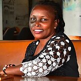 Porträtbild von Vicky Abenakyo (sitzend an einem Tisch)