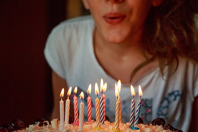 Frau pustet Geburtstagskerzen auf einem Kuchen aus