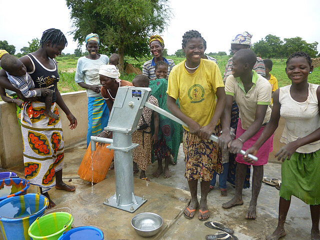 Junge Frauen, die gemeinsam Wasser an einem Brunnen pumpen und dabei lachen