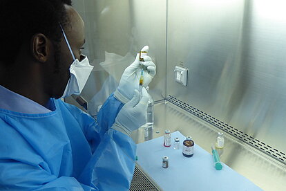 Ein Mann in blauer Schutzausrüstung befüllt eine Spritze mit Zytostatika. 