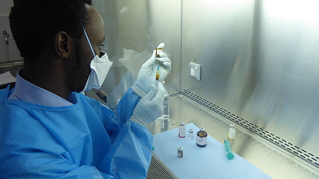 Ein Mann in blauer Schutzausrüstung befüllt eine Spritze mit Zytostatika. 